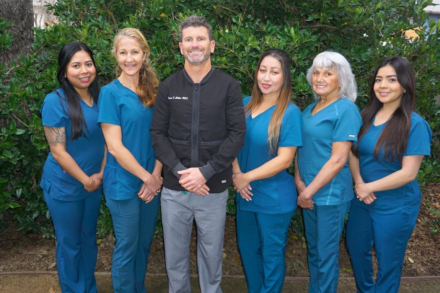 Dr. Kevin Miller with the Dentistry in Paradise team, in matching blue scrubs, outdoors in front of greenery.